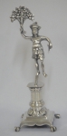 Paliteiro em prata brasileira provavelmente do séc. XIX, representando "Índio com cornucópia de flores sobre pedestal". Base trapezoidal. Pés de garra. Alt.: 17cm.