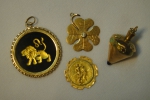 Quatro pendentes em ouro 18k representando "trevo de 4 folhas com brilhante", "signo de Leão com ônix", "mina" e "medalha sacra". Peso líquido: 7,5g. (Falta a argola da medalha sacra).