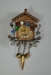 Antigo pendente no feitio de "relógio cuco" em ouro 14k, ornamentado com pedras coloridas. Alt.: 5,0cm.