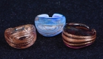 Três anéis em vidro moldado de Murano nas cores âmbar, marrom e azul salpicados com pó de ouro. Aros: 18, 15 e 19.