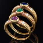 Três anéis em ouro 18k - 750mls contrastados com rubi, esmeralda e safira cabochon, guarnecidos com 2 brilhantes cada. Aro: 17. Peso: 8,9g.