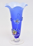 Vaso em vidro opalinado de "Murano" em double azul e branco leitoso. Corpo com aplicações de flores em relevo com núcleo em policromia. Borda de babado. Alt.: 21cm. (Em função da fragilidade, este lote só poderá ser enviado para fora do estado através de transportadora especializada).