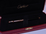 CARTIER. Elegante caneta esferográfica francesa da marca "Cartier" em baquelite negro arrematado em plaque d'or rajado. Parte superior guarnecida com rubi cabochon. Acompanha estojo original.