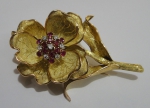 Broche no feitio de "ramo de flor" com pétalas articuladas em ouro 18k, 7 brilhantes e 12 pedras vermelhas provavelmente rubis. Alt.: 7,5cm. Peso: 36,7g.