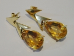 Par de brincos pendentes em ouro 18k, decorados com 2 "V" invertidos e guarnecidos com topázio gota. Alt.: 4cm. Peso: 12,6g.
