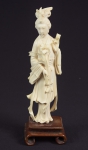 Figura esculpida em marfim, representado "Divindade Kuan Yin com ramo de flores". Base em madeira. Alt.: 27cm. China - 1900.