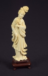 Figura esculpida em marfim, representado "Divindade Kuan Yin com flor de lótus e colar". Base em madeira. Alt.: 18cm. China - 1900.