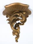 Peanha em madeira revestida com pátina dourada e entalhada em plumagens e volutas. Alt.: 29cm.