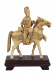 Grupo esculpido em marfim, representando "Guerreiro em Campo de Batalha sobre Cavalo". Base em madeira lavrada. Comp.: 21cm. Alt.: 15cm. Reproduzido com foto no catálogo.