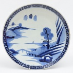 Medalhão em porcelana chinesa (circa 1900), esmaltado em azul e branco no padrão "Macau". Borda circundada com raminhos. Diâm.: 37cm. (Pequeno colado e fio de cabelo na borda). (Em função da fragilidade, este lote só poderá ser enviado para fora do estado através de transportadora especializada).