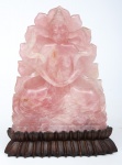 Figura esculpida em quartzo rosa representando "Buddah em Meditação". Base em madeira no formato de flor de lótus. Alt.: 22,5cm. (Pequeno lascado na lateral).