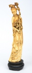 Figura esculpida em marfim, representando "Divindade Kuan Yin com ramos de peônias". Base em madeira. Alt.: 30cm. Apresenta "Selo Vermelho" na parte inferior gravado. China - séc. XIX.