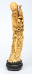 Figura esculpida em marfim, representando "Imortal com adereços, pêssegos e cesto de palha". Base em madeira. Alt.: 30cm. Apresenta "Selo Vermelho" na parte inferior gravado. China - séc. XIX.