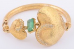 Pulseira em ouro escovado decorada com 2 corações interrompidos por esmeralda baguete central de aproximadamente 3ct e 50 brilhantes laterais. Peso: 40,1g.
