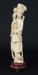 Figura esculpida em marfim, representando "Divindade Kuan Yin com ramo de peônia e abano". Base em madeira trabalhada. Alt.: 27cm. China - 1940.