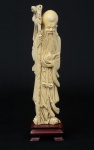 Figura esculpida em marfim, representando "Imortal com cajado e Pêssego". Base em madeira trabalhada. Alt.: 23cm. China - 1930.