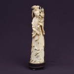 Figura esculpida em marfim, representado "Divindade Kuan Yin com ramos de peônia". Base em madeira. Alt.: 29cm. China - 1900. (Pequeno lascado no galho superior da peônia).