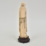 "Monge com cordão de pérolas nas mãos" esculpido em marfim. Base em madeira ricamente vazada e entalhada. Alt.: 29cm. China - 1940.